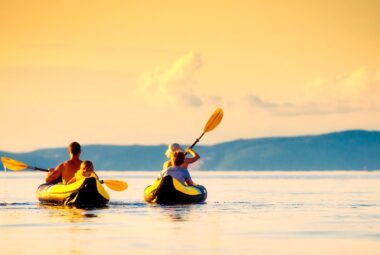 Family riding two kayaks into the sunset on a lake